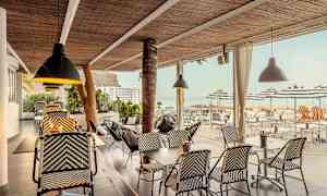 En utendørsservering med rottingmøbler og taklamper, utsikt mot havet og parasoller. (AI-generert tekst)