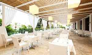 Restaurant med hvite bord og stoler under tak nær grøntområder. (AI-generert tekst)