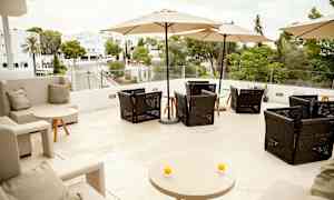 Terrasse med sitteplasser og parasoller, utsikt mot grøntområder og bygninger. (AI-generert tekst)