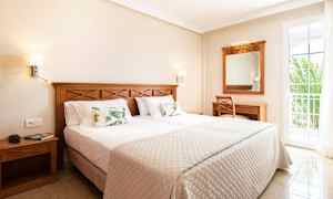 Et hotellrom med en dobbeltseng, treinnredning og en balkongdør. (AI-generert tekst)