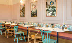 En restaurant med bord og stoler, bilder på veggen og myke sofaer langs veggen. (AI-generert tekst)