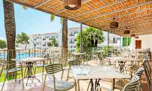 Terrasse med bord og stoler, et basseng og hotellbygninger i bakgrunnen. (AI-generert tekst)