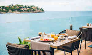 Dekket spisebord med tallerkener og glass på en terrasse med havutsikt. (AI-generert tekst)