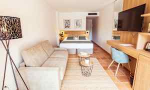 Et hotellrom med en sofa, en dobbeltseng, et skrivebord med en stol og en TV. (AI-generert tekst)