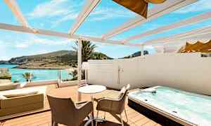 Terrasse med bord, stoler, boblebad og utsikt mot stranden og havet. (AI-generert tekst)