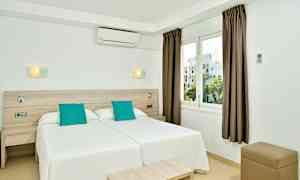 Et hotellrom med to enkeltsenger ved siden av hverandre, hvit innredning og turkise puter, samt et vindu med utsikt. (AI-generert tekst)