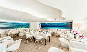 En moderne restaurant med hvite stoler og bord, samt et stort undervannsmaleri på veggen. (AI-generert tekst)