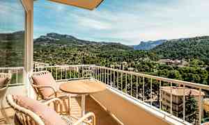 Utemøbler på en balkong med utsikt over en frodig dal og fjell i bakgrunnen. (AI-generert tekst)