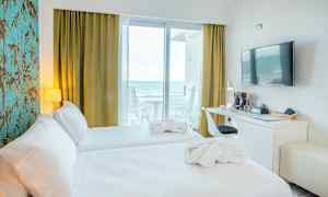 Hotellrom med to senger, skrivebord, vegg-TV og havutsikt fra balkongen. (AI-generert tekst)