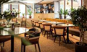 En moderne kafé med trebord og marmorbord, omgitt av grønne planter. (AI-generert tekst)