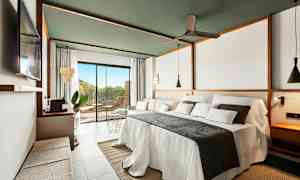 Et moderne hotellrom med en stor oppredd seng, sofa og et stort vindu mot en terrasse. (AI-generert tekst)