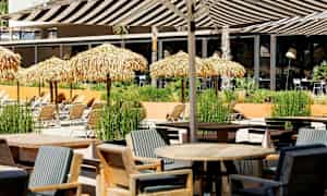 Et utendørsområde med bord, stoler og solsenger under stråtak. (AI-generert tekst)