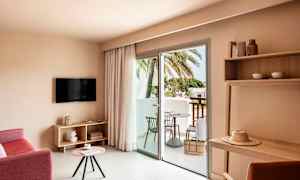 Hotellrom med sittegruppe, TV, bord og balkong med utsikt mot palmer. (AI-generert tekst)