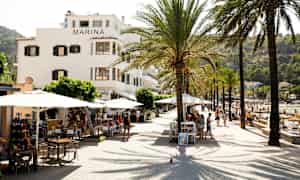 En gate med palmer, bord og bygningen Marina ved siden av en strand. (AI-generert tekst)