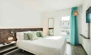 Et hotellrom med en dobbeltseng, dekorative puter, et vindu med turkise gardiner og en TV på veggen. (AI-generert tekst)