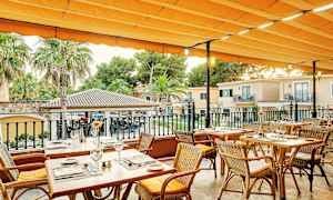 Utendørsterrasse med dekkede trebord og stoler under en oransje markise. (AI-generert tekst)