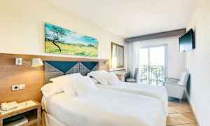 Et hotellrom med to enkeltsenger, lyse sengetepper, et maleri over sengegavlen, en liten balkong og en TV på veggen. (AI-generert tekst)