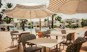 Utendørs bassengområde med solsenger, parasoller og bord med stoler. (AI-generert tekst)