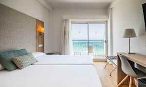 Hotellrom med to senger, skrivebord og utsikt over havet gjennom en glassdør. (AI-generert tekst)