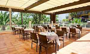 Uteservering med dekkede bord, stoler og hagemiljø i bakgrunnen. (AI-generert tekst)