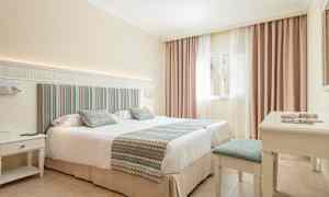 Hotellrom med en dobbeltseng, lyse farger og et vindu med gardiner. (AI-generert tekst)