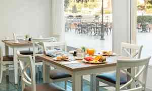 Et dekket bord med frokostmat, inkludert juice, brød og frukt, i en lys spisesal med vinduer mot en utendørsterrasse. (AI-generert tekst)