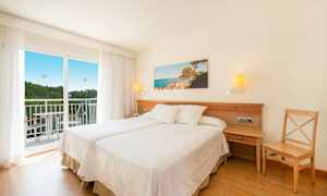 Et hotellrom med to enkeltsenger, en balkong og et landskapsbilde på veggen. (AI-generert tekst)