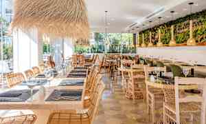 Restaurant med trebord, rottingstoler og dekorative lysarmaturer. (AI-generert tekst)