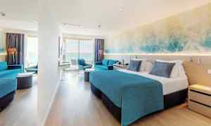 Et hotellrom med dobbeltseng, blå innredning og en sittegruppe. Et stort vindu gir utsikt over havet. (AI-generert tekst)