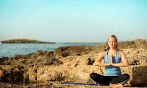 Person i treningsklær sitter i meditasjonsstilling på en klippe ved havet. (AI-generert tekst)