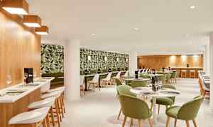 Et restaurantinteriør med grønmalte stoler og en tapetert vegg med planteprint. (AI-generert tekst)