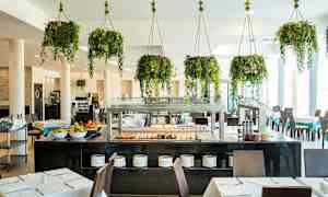 Restaurant med bord, stoler og buffet samt hengende grønne planter. (AI-generert tekst)