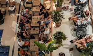 En gruppe mennesker sitter ved bord og sofaer i en utendørs lounge. (AI-generert tekst)