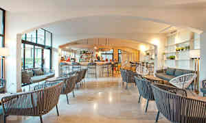 Interiør av en moderne lounge med bar, hvor flere sittegrupper er plassert med stoler og sofaer i et lyst og luftig rom. (AI-generert tekst)