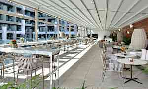 Et moderne og lyst innredet terrasse- eller restaurantområde med glassvegger, rekker av bord og stoler samt dekorative planter. (AI-generert tekst)