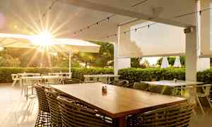 Utendørs restaurant med solstråler gjennom parasoller og grøntområde. (AI-generert tekst)