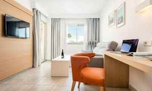 Lyst, moderne hotellrom med sofa, stol, TV, skrivebord og store vinduer. (AI-generert tekst)