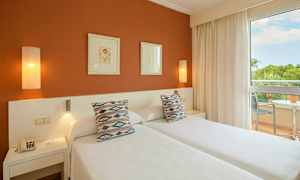 Bilde av et hotellrom med to enkeltsenger, pynteputer, kunst på veggen og en balkong med utsikt. (AI-generert tekst)