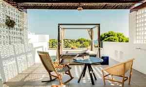 En terrasse med to stoler og et lite bord samt en dagseng med utsikt over vegetasjon og hav. (AI-generert tekst)