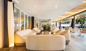 Et avslapningsområde med hvite sofaer og bord, omgitt av glassvegger og moderne møbler. (AI-generert tekst)