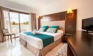 Et hotellrom med to enkeltsenger, en TV og en balkong i bakgrunnen. (AI-generert tekst)