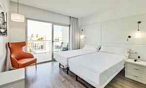 Et lyst og moderne hotellrom med to enkeltsenger, en oransje lenestol og et glassvindu som fører til en balkong. (AI-generert tekst)