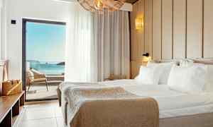 Et hotellrom med en stor seng og havutsikt gjennom en balkongdør. (AI-generert tekst)