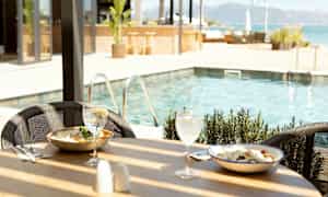 Spisebord ved siden av bassenget med to retter og drikker. (AI-generert tekst)