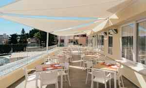 En terrasse med bord og stoler under solskjermtak. (AI-generert tekst)