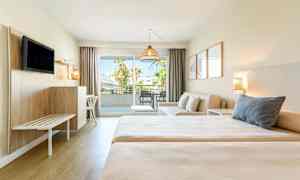 Et hotellrom med to senger, en sittegruppe og balkong med utsikt. (AI-generert tekst)