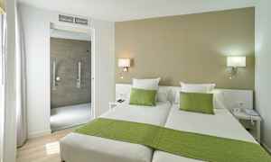 Hotellrom med to enkeltsenger, grønt sengetøy og en åpning mot badet. (AI-generert tekst)