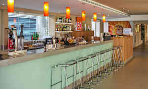 En moderne bardisk med barkrakker samt flasker og glass på hyller og benker. (AI-generert tekst)