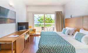 Hotellrom med to senger, skrivebord og vindu med utsikt mot balkong. (AI-generert tekst)