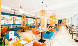 Bilde av en moderne restaurant med fargerike stoler, trebord og dekorative lysarmaturer. (AI-generert tekst)